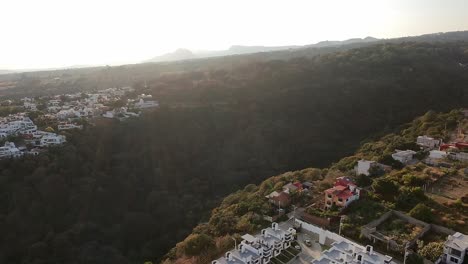 drone shot of hillside neighborhoods and forested canyon in cuernavaca, morelos. white and red-roofed houses line the edges of a deep green ravine under golden afternoon light