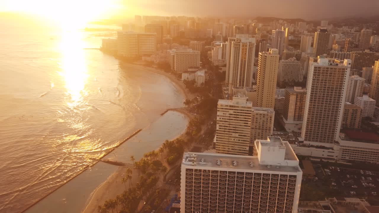 Drone aéreo panorâmico voando lentamente sobre o colorido horizonte de Honolulu durante o pôr do sol em Oahu, Havaí, com a Praia de Waikiki como um ponto de interesse especial