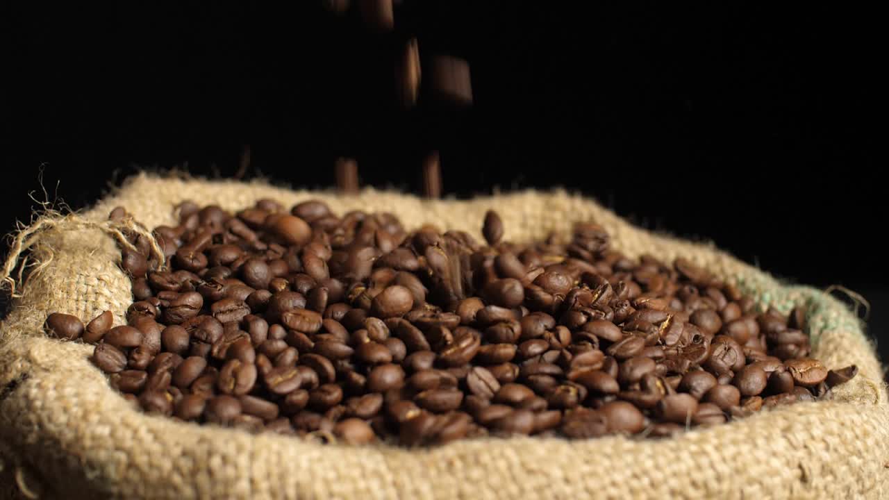 Chicchi di caffè tostati che cadono su un mucchio di chicchi in un sacco, slow motion