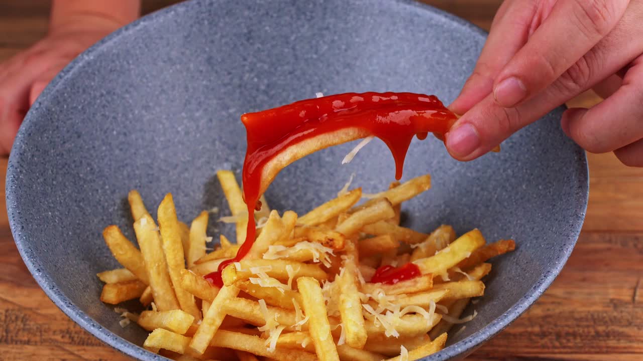Close up of a pair of French fries with grated cheese being bathed in ketchup