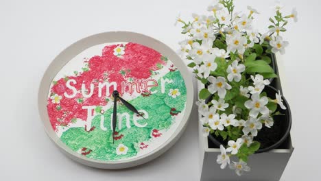 clock and box with flowers stands on a white table , time lapse