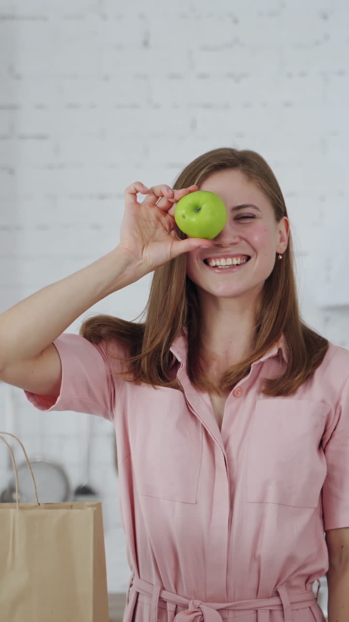 Beautiful woman holding green apples on kitchen background. Happy female closing her eyes by two fresh apples indoors. Dieting concept. Vertical video