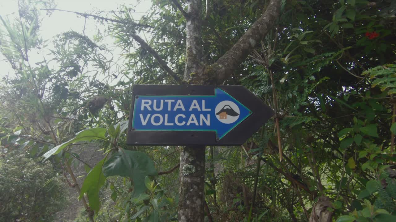 Sign points to a lush green path leading to Tungurahua volcano, Ecuador, surrounded by dense vegetation