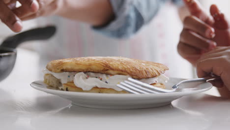 close up of grandfather in kitchen serving pancake filled with cream for grandson to eat