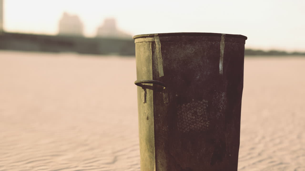 Forgotten trash can stands alone on a deserted sandy landscape at dusk