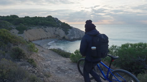 ciclista empujando bicicleta a lo largo del acantilado con una impresionante vista de la playa a primera hora de la mañana.