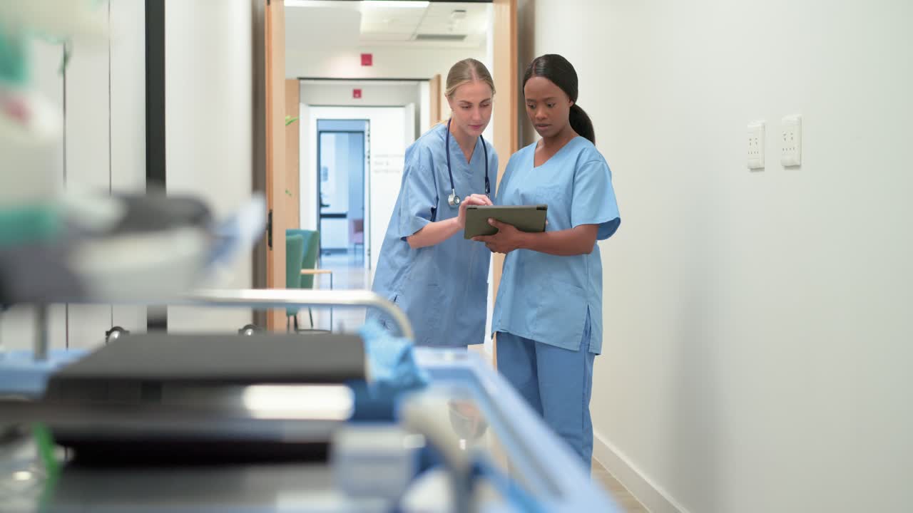 Diverse female nurses entering doorway in scrubs, walking and consulting tablet for care
