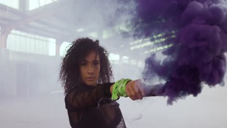 Female-dancer-in-an-empty-warehouse-holding-smoke-grenade