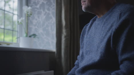 unhappy mature man trying to keep warm by radiator at home during cost of living energy crisis