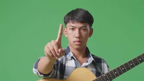 close up of asian teenager with guitar showing no gesture while standing on green screen background