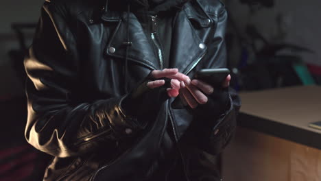 hacker wearing mask using phone dressed in leather jacker and gloves