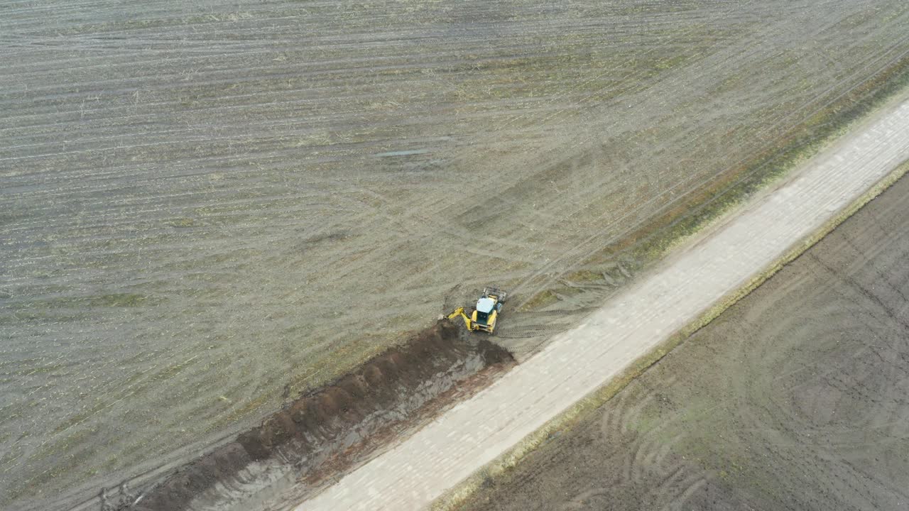 aproximación aérea hacia el tractor excavadora cavar sistema de drenaje de zanja cerca de la carretera
