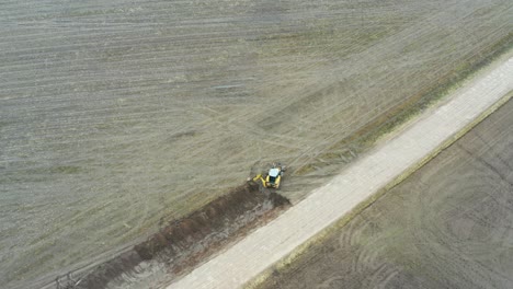 Luftaufnahme-Eines-Traktor-Baggers,-Der-Ein-Entwässerungssystem-Für-Gräben-In-Der-Nähe-Der-Straße-Gräbt