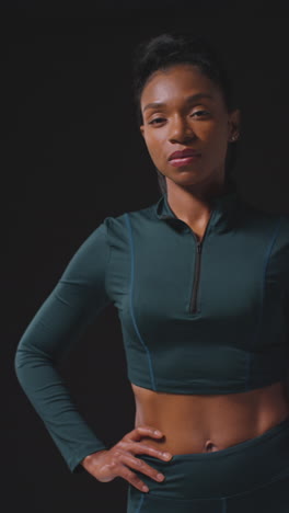 vertical video portrait of serious female athlete wearing tracksuit training for sports event against black studio background