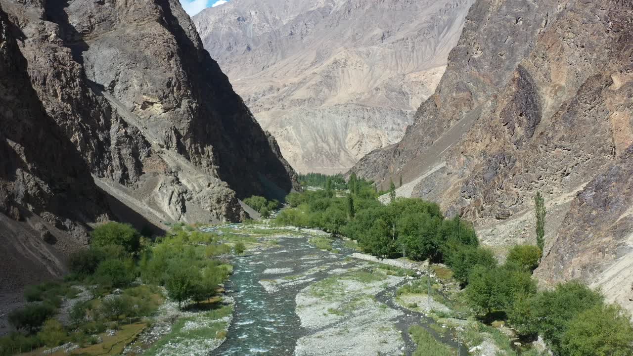 drone aéreo volando a través de un gran y hermoso valle del cañón rodeado de montañas a ambos lados y un río debajo que fluye desde la cascada artificial manthokha en skardu pakistán en un día soleado