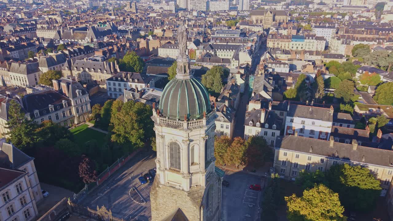 Drone orbiting the church tower and statue in Rennes under morning sunlight