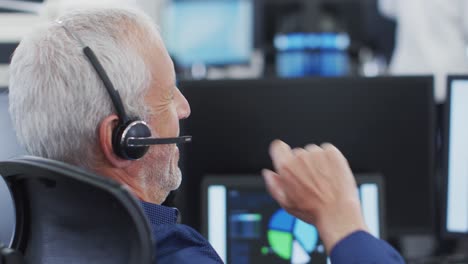 Man-wearing-headset-talking-while-sitting-on-his-desk-at-office