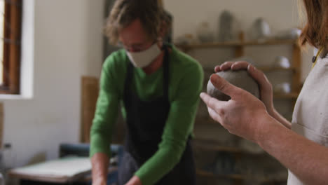 male and female potter wearing face mask and apron kneading the clay at pottery studio