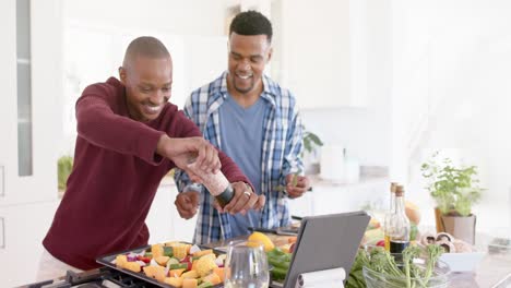 happy african american gay male couple preparing dinner, seasoning vegetables, slow motion