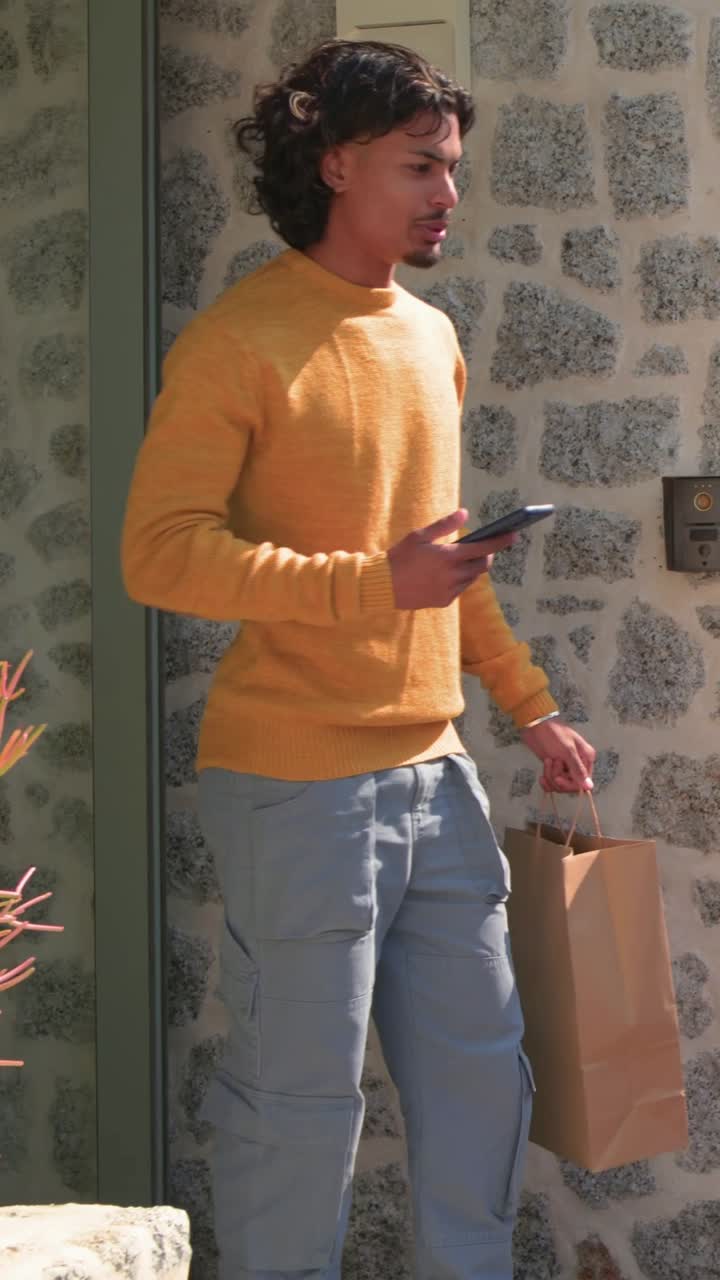 Vertical video: Picking up bag after drop, man in mustard knit holding phone tapping reader at door