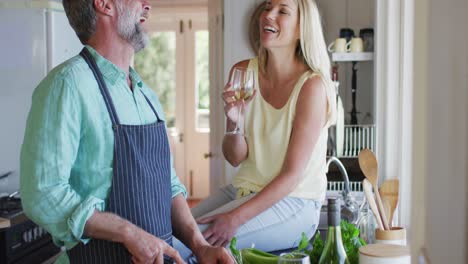 happy caucasian mature couple cooking together and drinking wine in the kitchen