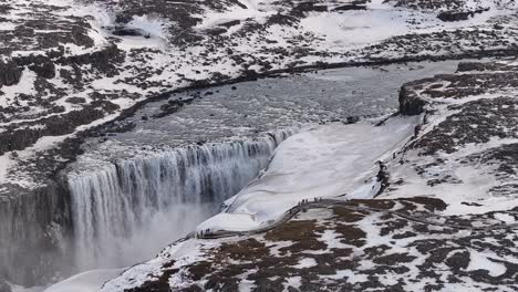 Tourists gather on snowy cliffs overlooking Dettifoss waterfall in Iceland’s frozen north