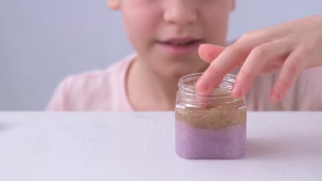 the child's hands are close-up. a child of primary school age takes the slime out of the jar. a slic of different colors. the child lays out the toy on the table in front of him. touch, emotion