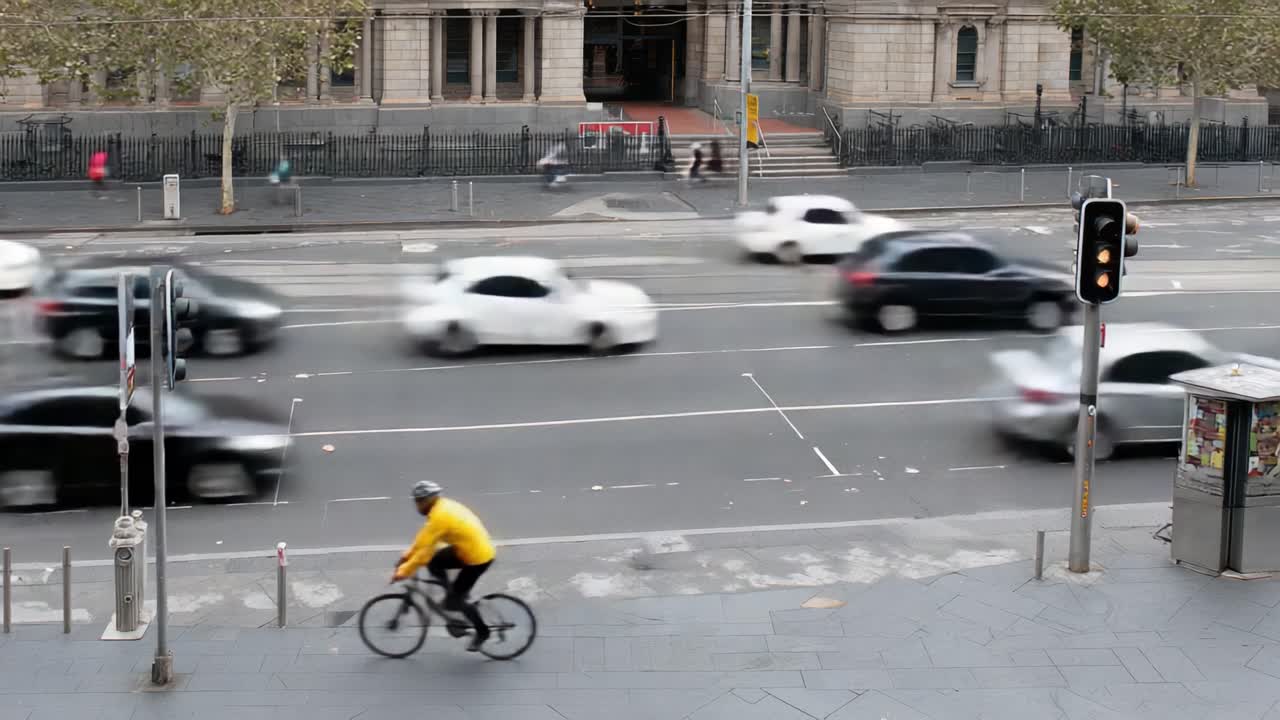 A cyclist in a bright yellow jacket navigates a busy city street as cars rush by, highlighting the contrast between slower pedal power and fast urban traffic in motion