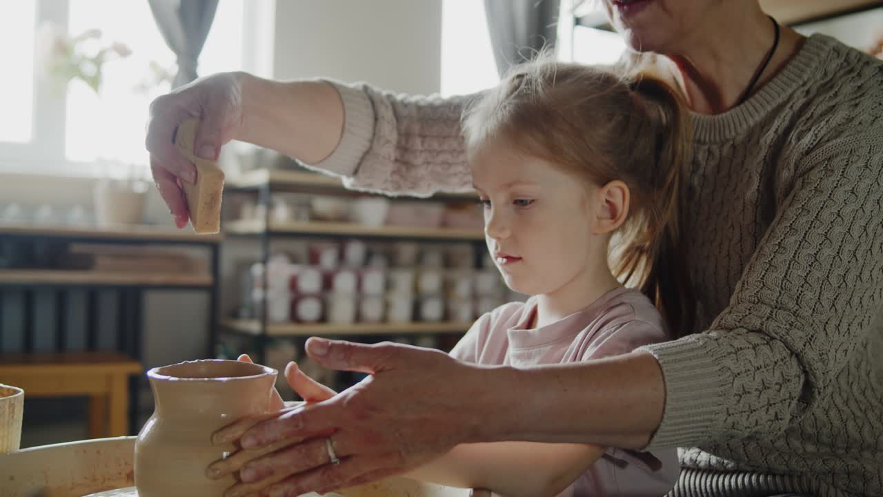 la abuela enseña a su nieta a trabajar en una rueda giratoria de cerámica