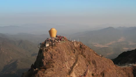 Fly-backwards-from-the-top-of-the-mountain-with-numerous-tourists-on-top,-with-mountain-ridge-in-background-in-afternoon