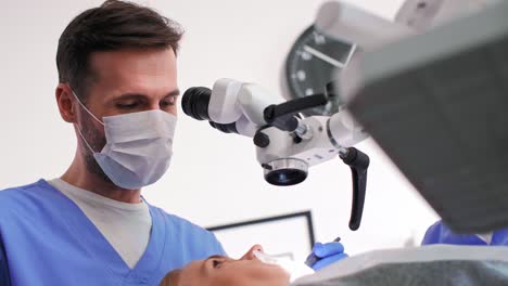 dentist using dental microscope and examining woman's teeth