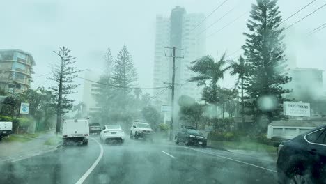 los vehículos navegan por calles empapadas de lluvia mientras el ciclón alfred se acerca a gold coast, australia, bajo cielos nublados y árboles balanceados.