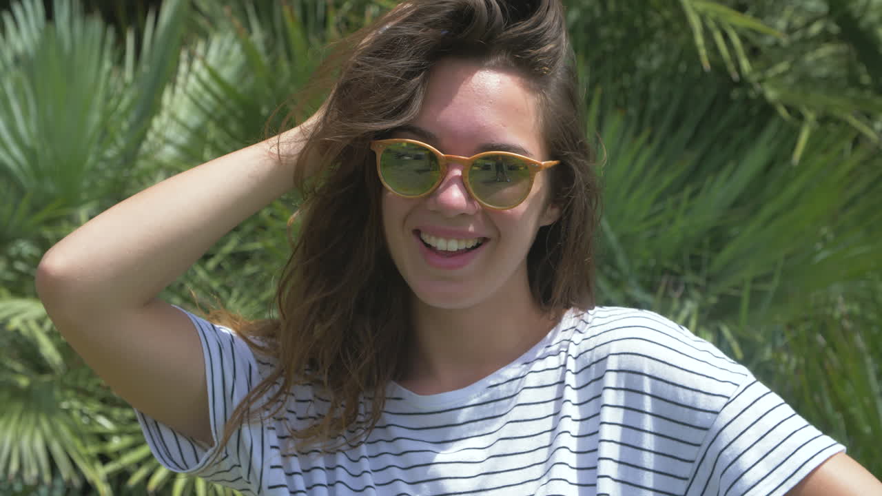 una mujer joven con gafas de sol sonriendo frente a las palmeras