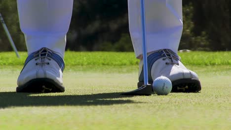 primer plano de los zapatos de los golfistas y el club de golf golpeando la bola en la parte superior verde