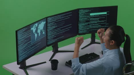 vista lateral de una desarrolladora asiática feliz celebrando y bailando mientras escribe código con múltiples pantallas de computadora en el estudio de pantalla verde