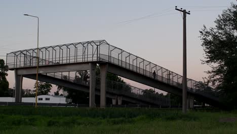 A-woman-walks-down-a-pedestrian-bridge-crossing-over-a-National-Route-at-Firmat,-Santa-Fe,-Argentina