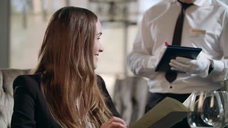 smiling woman talking with waiter in restaurant. happy woman reading menu