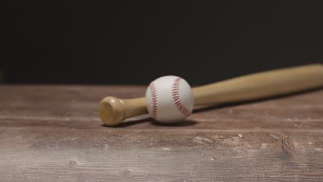 studio baseball shot with person picking up wooden bat and ball from wooden background