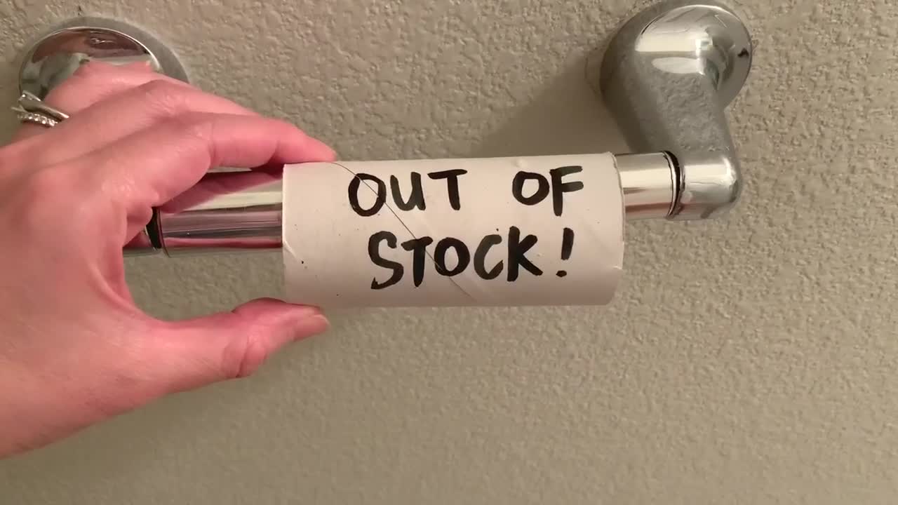 Person reading the words "OUT OF STOCK" written over an empty toilet paper roll. POV shot. Camera slowly zooms in at the text.