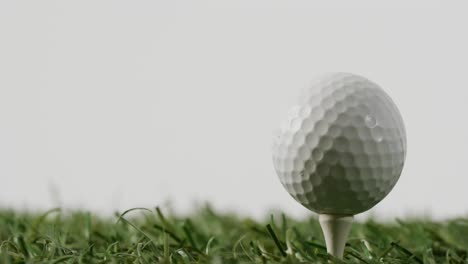 Close-up-of-golf-tee-and-ball-on-grass-and-white-background,-copy-space,-slow-motion