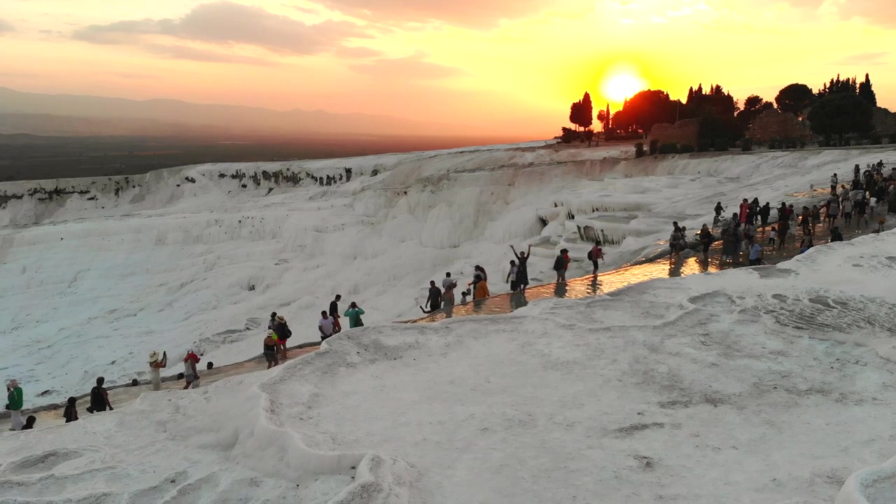 Turister går på hvide travertinterrasser i Pamukkale ved solnedgang