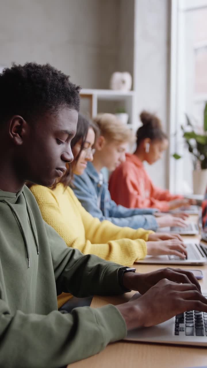 Side angle video of diverse students focused on laptops in a bright, modern classroom