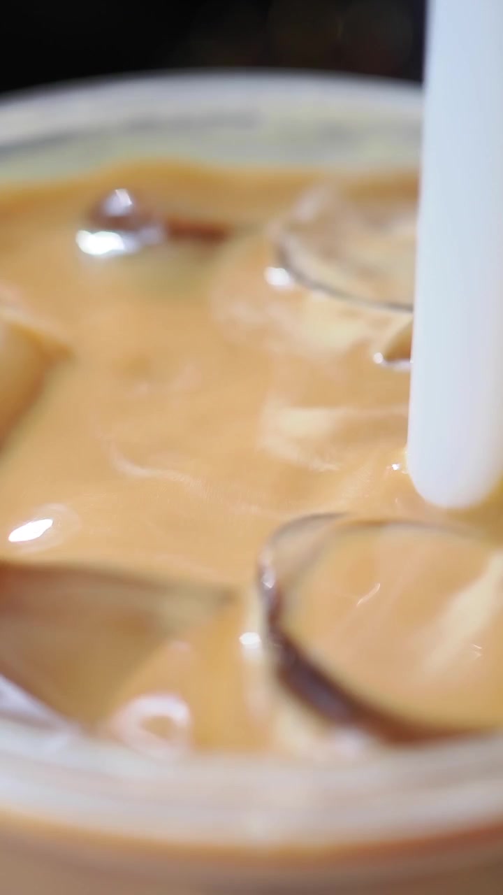 Close-up of a Hand Stirring Iced Coffee with a Straw