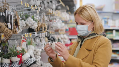 a young woman in a protective mask chooses christmas tree toys in the store