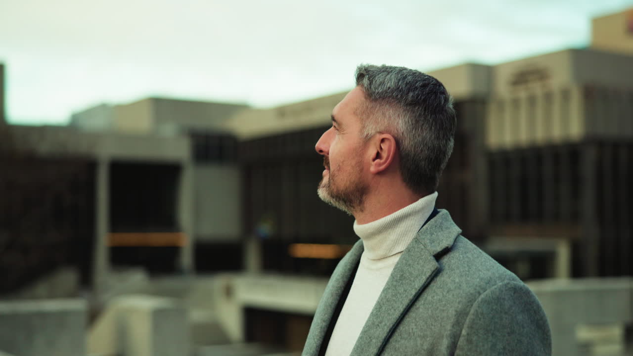Mature man with gray hair and beard wearing coat and turtleneck looking up outdoors
