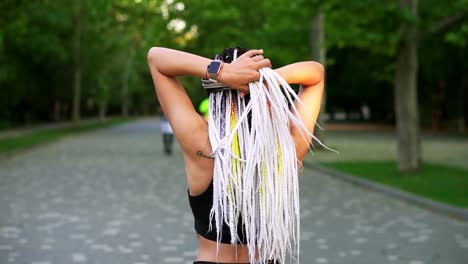 black and white dreadlocks on the back of a girl. rear view of a sporty girl knotting hair and starting to run in the green