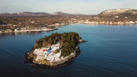 aerial footage flying to the right past a snow covered curtis island lighthouse with camden harbor in the background