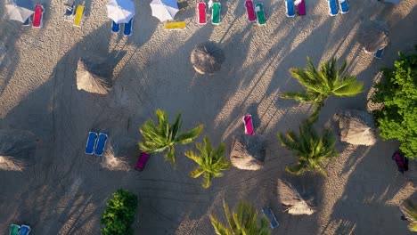 Das-Licht-Des-Sonnenaufgangs-Verbreitet-Lange-Schatten-Von-Palmen-Und-Strandkörben-über-Den-Sand-Im-Karibischen-Inselparadies