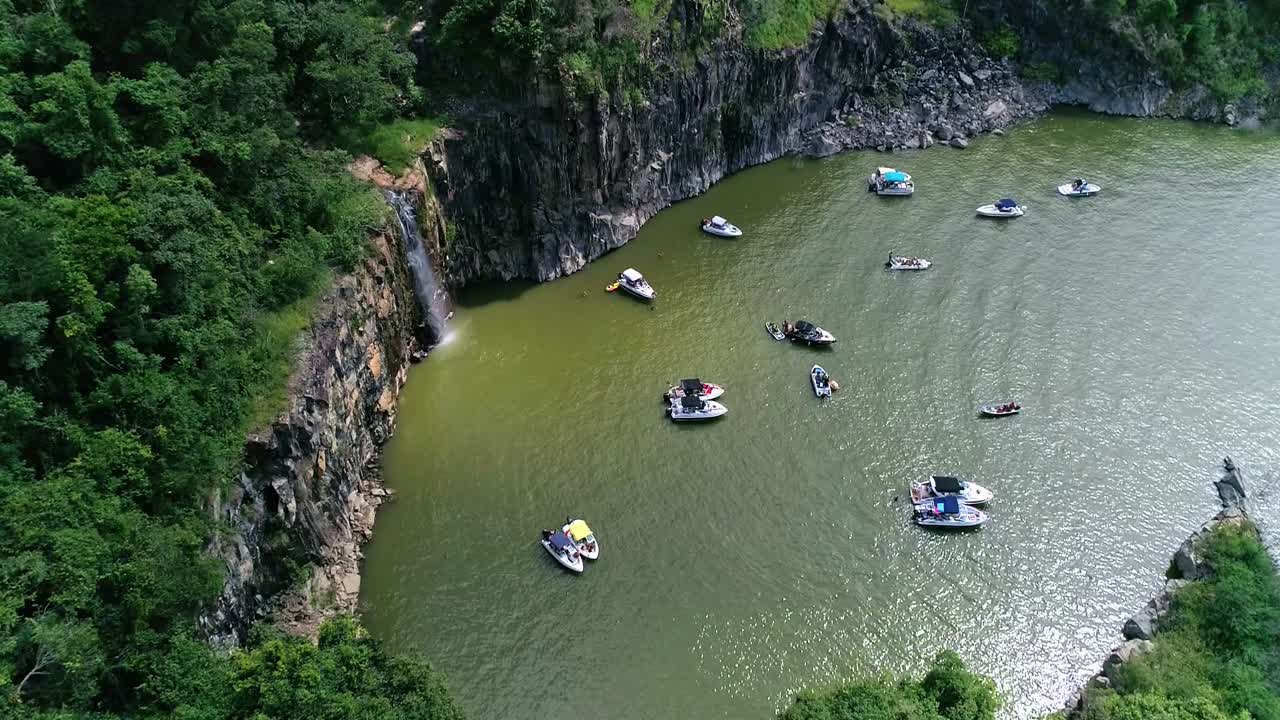 Boats anchored on coast near waterfall falling into sea waters. Aerial