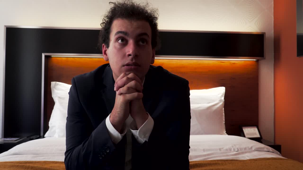 Uomo d'affari in viaggio che prega sul letto della camera d'hotel.